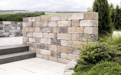 Mauer aus hellen, rechteckigen Steinen am Gartenbeet neben Treppe und Pflasterfläche