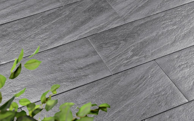 Graue Terrassenplatten mit quarzitartiger Oberfläche und diagonaler Verlegung, im Vordergrund grüne Blätter