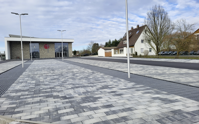 Gepflasterte Außenanlage mit grauen, nuancierten Pflastersteinen und dunklen Streifen entlang der Fläche