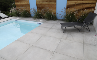 Graue Terrassenplatten an einem Pool mit Liegen und Holzsichtschutz