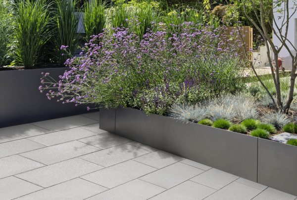Graue Terrassenplatten neben erhöhten Pflanzbeeten im Garten