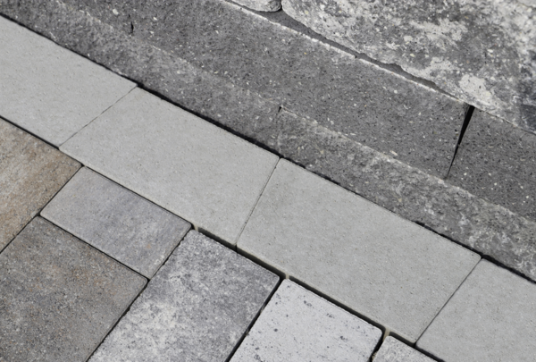 Graue Mähkante als Beeteinfassung zwischen Pflastersteinen und Natursteinmauer
