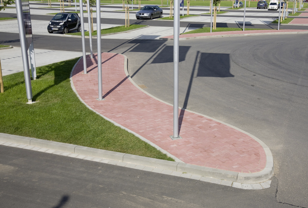 Bordstein-Absenker aus grauem Beton, rund verlegt an einer rot gepflasterten Verkehrsinsel im Außenbereich
