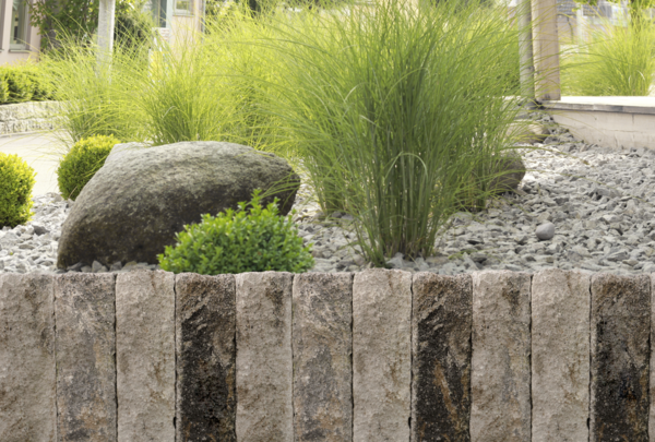 Natursteinmauer vor Kiesbeet mit Gräsern und Bepflanzung im Garten
