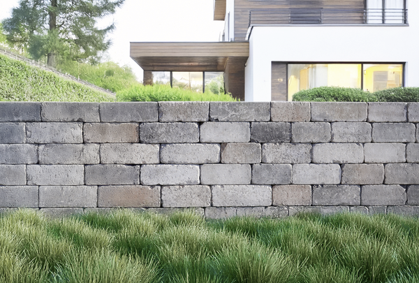 Natursteinmauer aus grauen Quadern vor einem Garten mit Haus und Rasen