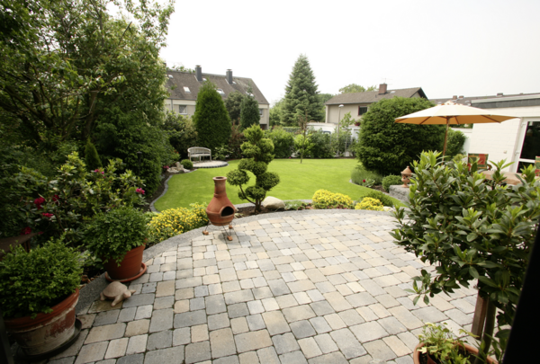 Pflaster aus grauen Betonsteinen für Terrasse und Gartenweg im begrünten Garten