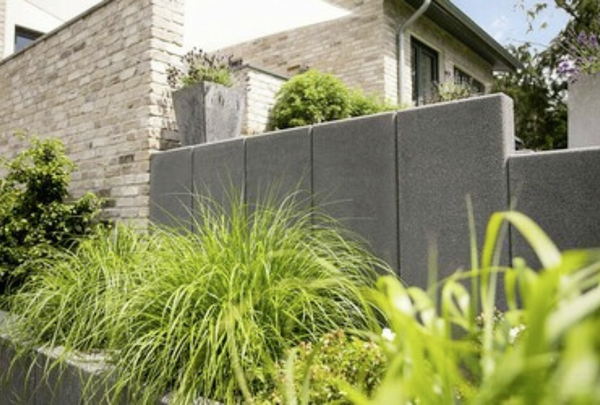 Anthrazitfarbene Stützwinkel-Mauer als Gartenbegrenzung mit bepflanzter Außenanlage