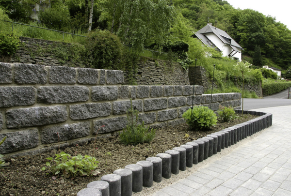 Kleine Verbundpalisaden als Beeteinfassung entlang eines gepflasterten Weges, graues Produkt im Gartenbereich
