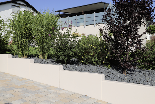 Beiger Stützwinkel als niedrige Mauer am bepflanzten Gartenbeet neben Pflasterfläche