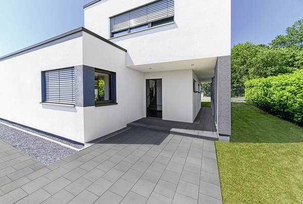 Graue Pflastersteine auf der Terrasse vor einem modernen Haus, mit Gartenweg und Rasen