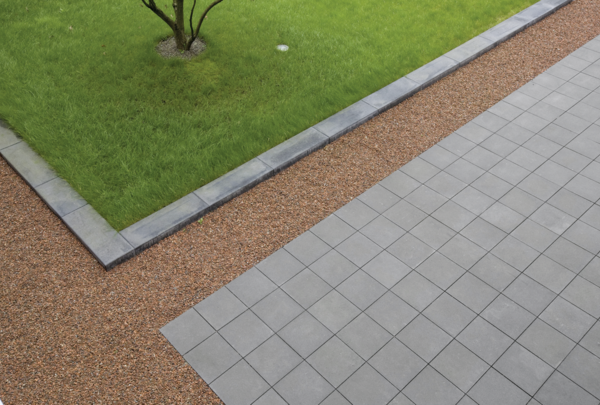Grau verlegte Gehwegplatten mit feiner Rasterung an einer Gartenfläche