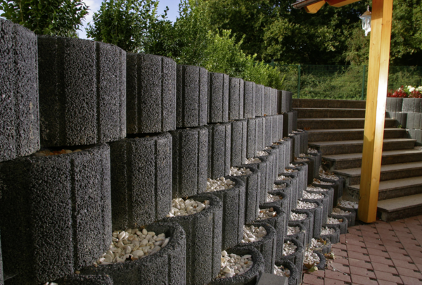 Anthrazitfarbene Hangflor-Elemente als gestufte Stützmauer mit Steinen im Garten