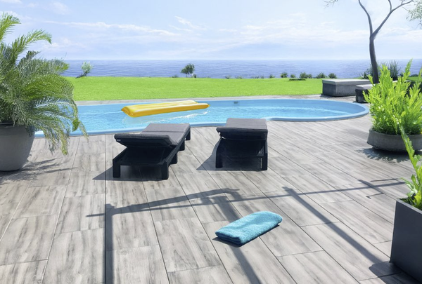Großformatige graue Terrassenplatten am Pool mit Liegen und Meerblick