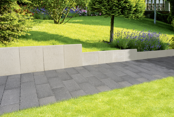 Graue L-Steine als Gartenmauer neben einem gepflasterten Weg im Garten