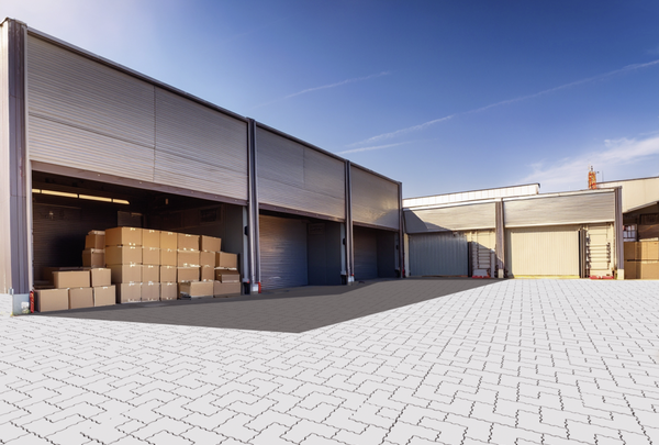 graue Pflasterfläche in Industriehof mit Lagerhallen und gestapelten Kartons