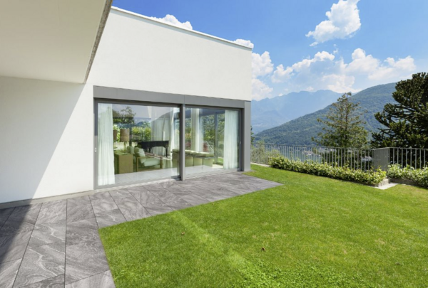 Terrassenplatten in Grau, vor moderner Terrasse mit Rasen und Bergblick