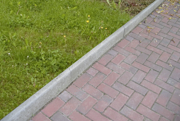 Graue Rasenkante als Beetbegrenzung am gepflasterten Gartenweg