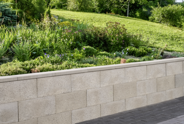 Grau gemauerte Mauer mit Abdeckplatte vor bepflanzter Gartenanlage und gepflastertem Weg