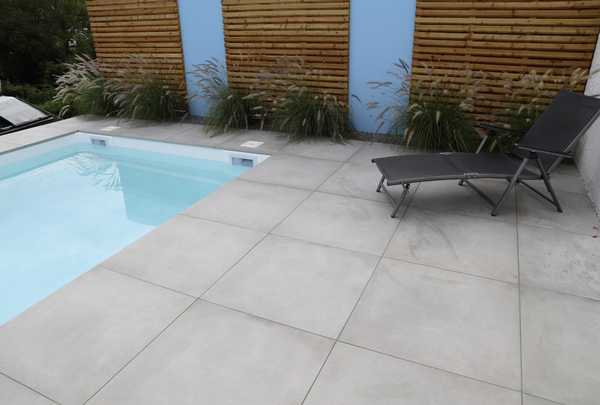 Graue Terrassenplatten an einem Pool mit Liegen und Holzsichtschutz