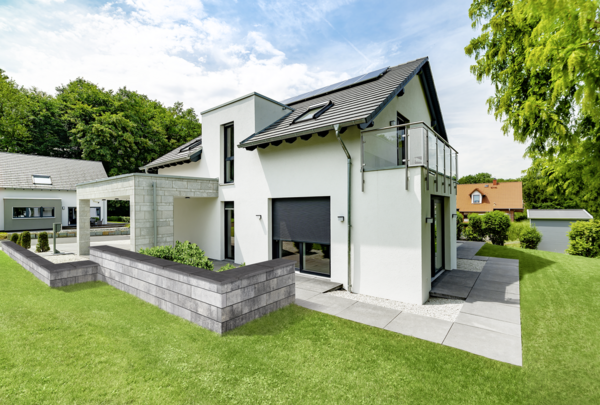 Graue Mauer als Hochbeet vor modernem Haus mit Terrasse und Gartenweg, Tribus