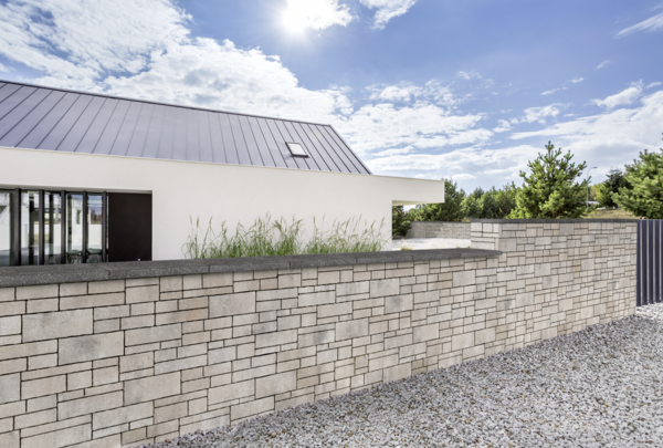 Tribus-Mauer aus hellen Quadern vor modernem Haus und Kiesfläche im Garten