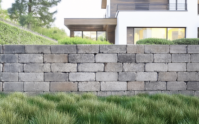 Mauer aus grauen Quadern vor einem Garten mit Haus und Rasen