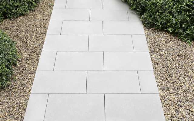 Graue Betonplatten auf Gartenweg zwischen Kiesflächen und Hecken