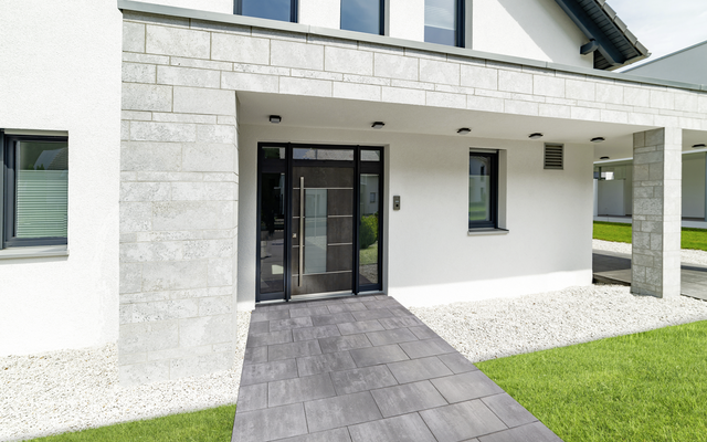 Grau-anthrazitfarbene Terrassenplatten vor Hauseingang und Außenanlage, mit hellen Steinflächen und Rasen
