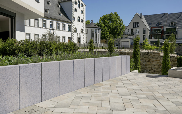 Pflastersteine in hellgrauer Verlegung auf Terrasse vor Gartenmauer und Wohngebäuden