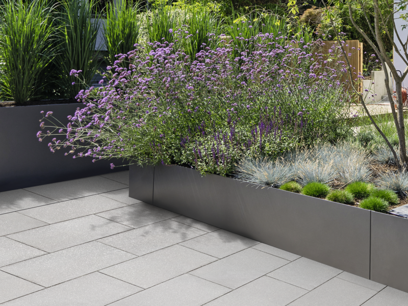 Graue Terrassenplatten neben erhöhten Pflanzbeeten im Garten