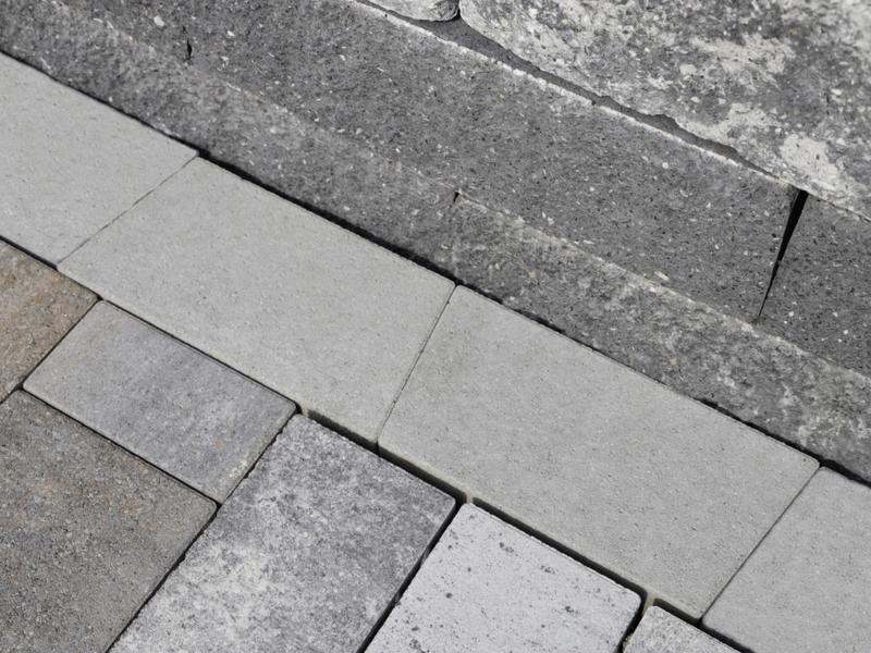 Graue Mähkante als Beeteinfassung zwischen Pflastersteinen und Natursteinmauer
