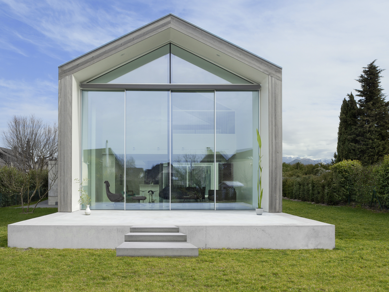 Moderne Gartenlounge mit großer Glasfront und heller Stufenanlage vor einer Rasenfläche