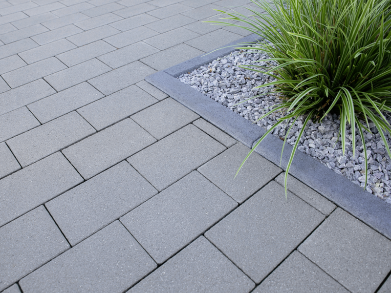 Graue Pflastersteine auf Terrasse mit Beetrand aus Beton und Kies