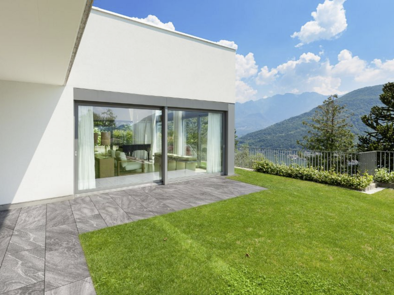Terrassenplatten in Grau, vor moderner Terrasse mit Rasen und Bergblick