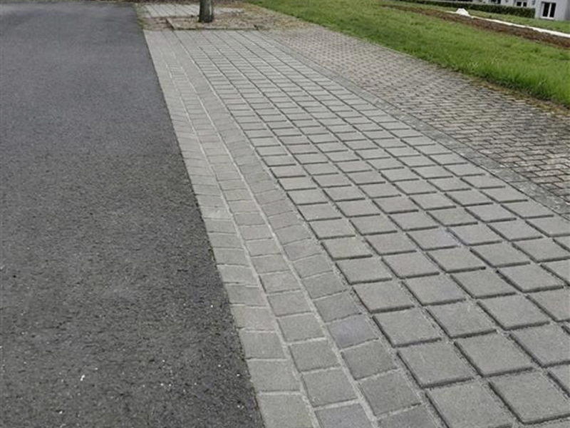 graues Rinnenpflaster entlang einer Straße und eines Gehwegs am Ortsrand