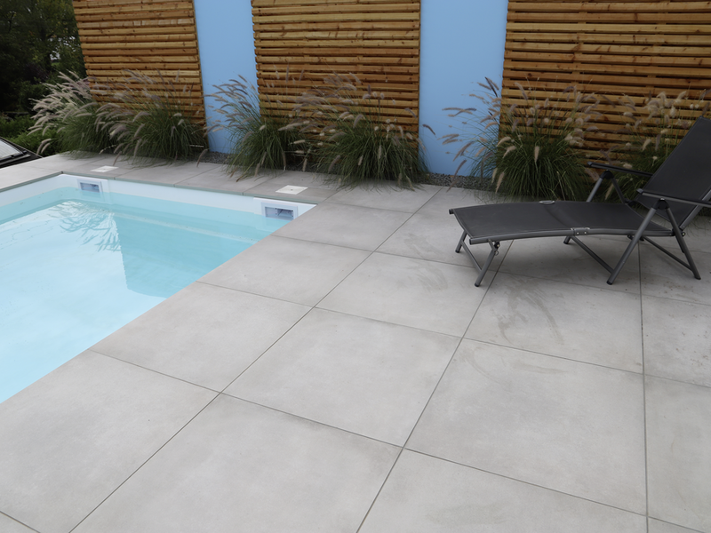 Graue Terrassenplatten an einem Pool mit Liegen und Holzsichtschutz