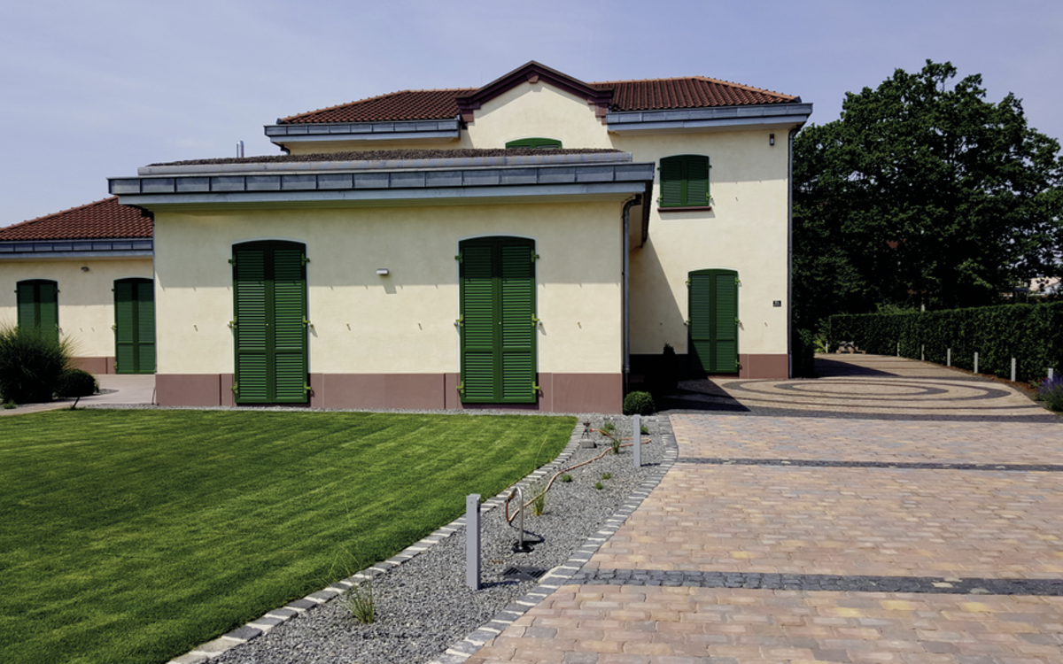 Pflastersteine in Altstadtfarben für die Einfahrt vor einem Haus mit Rasen und Kiesstreifen
