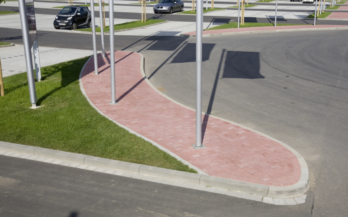 Bordstein-Absenker aus grauem Beton, rund verlegt an einer rot gepflasterten Verkehrsinsel im Außenbereich