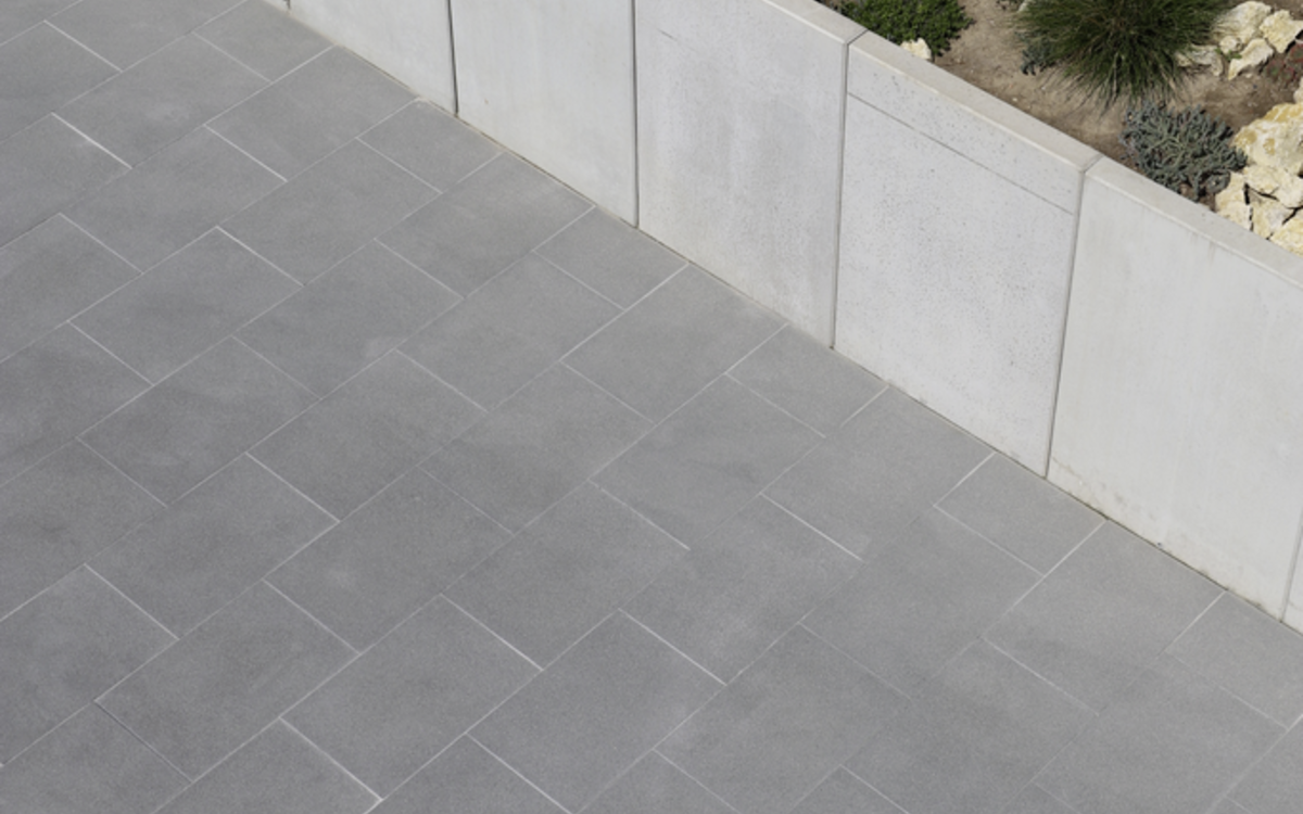 Graues Pflaster in der Außenanlage neben einer hellen Stützwand aus Betonplatten und Kiesbeet