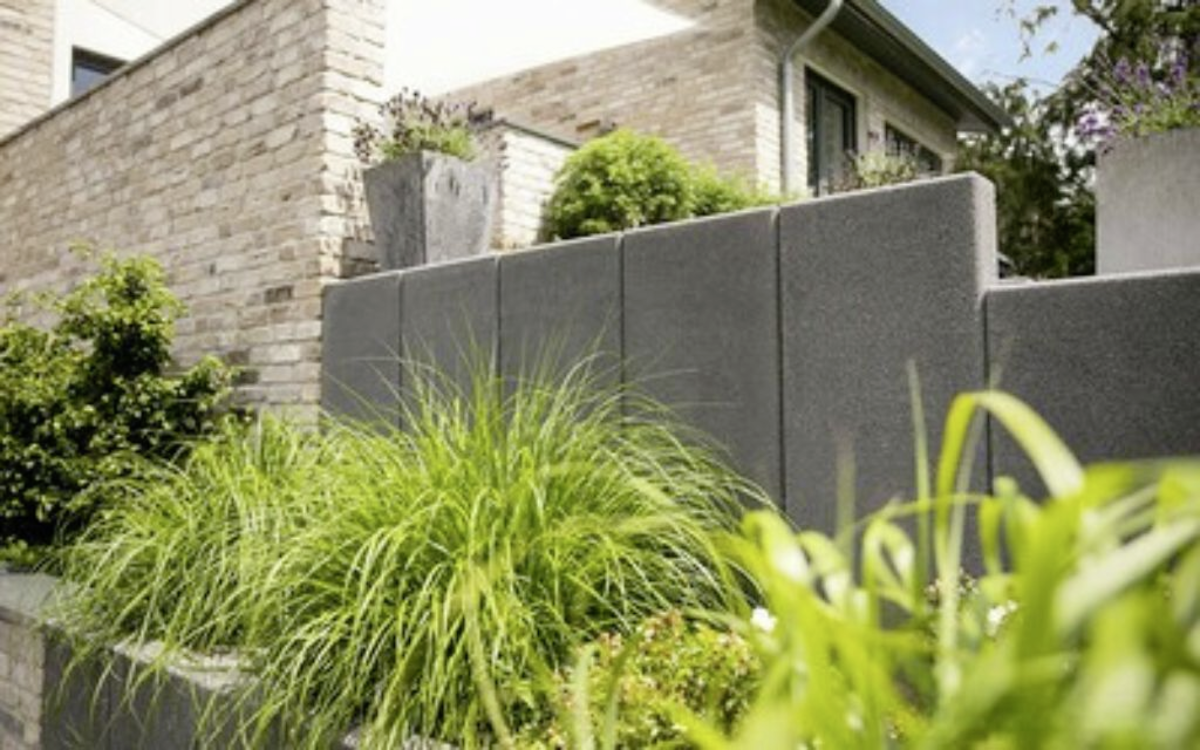 Anthrazitfarbene Stützwinkel-Mauer als Gartenbegrenzung mit bepflanzter Außenanlage