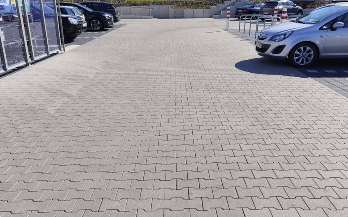 Doppel-T-Pflaster auf Parkplatzfläche, grau verlegt, mit Autos und Bäumen im Hintergrund