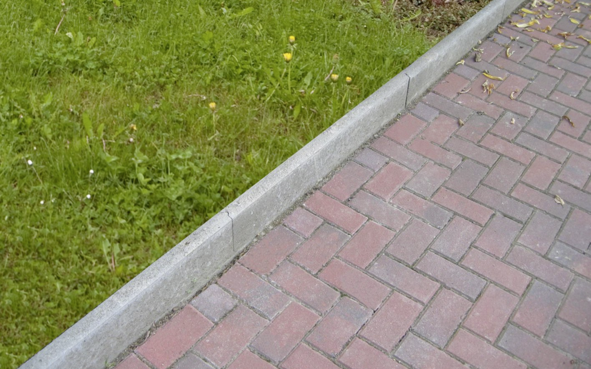 Graue Rasenkante als Beetbegrenzung am gepflasterten Gartenweg