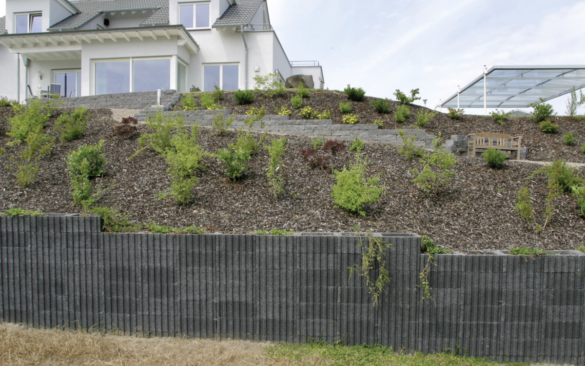 Gestufte Gartenmauer aus anthrazitfarbenen Betonsteinen mit bepflanzter Böschung, Rasterflor