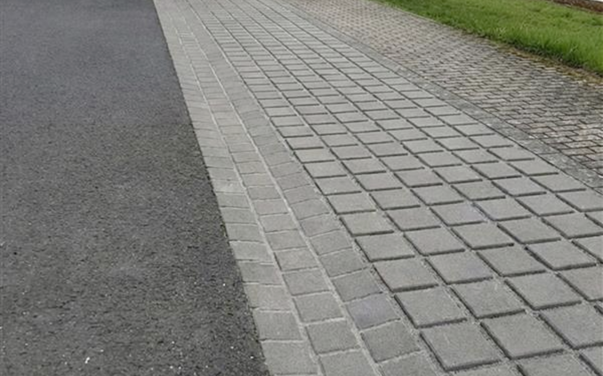 graues Rinnenpflaster entlang einer Straße und eines Gehwegs am Ortsrand
